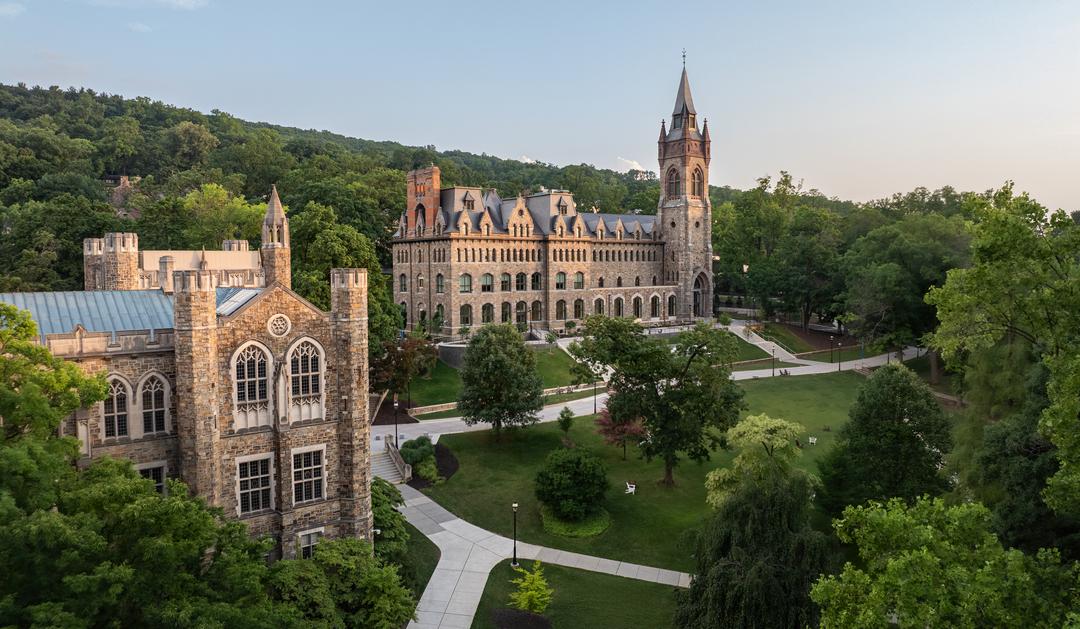 Photograph of Gothic stone campus buildings surrounded by lush green trees and hills.