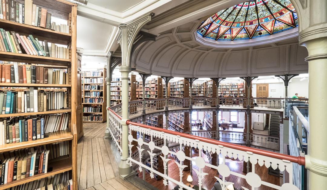 Photograph of a circular library with a stained-glass dome and wooden bookshelves.