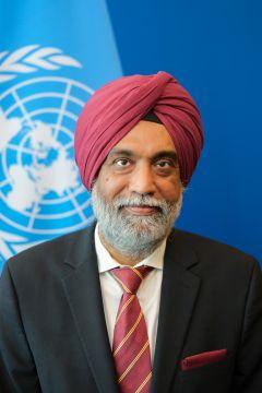 Photograph of a man in a red turban and suit in front of the United Nations flag.