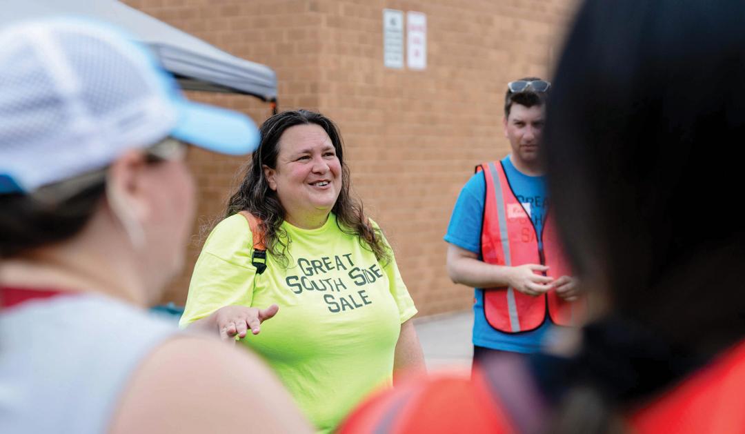 Photograph of a smiling woman in a lime green shirt talking to a group outdoors.