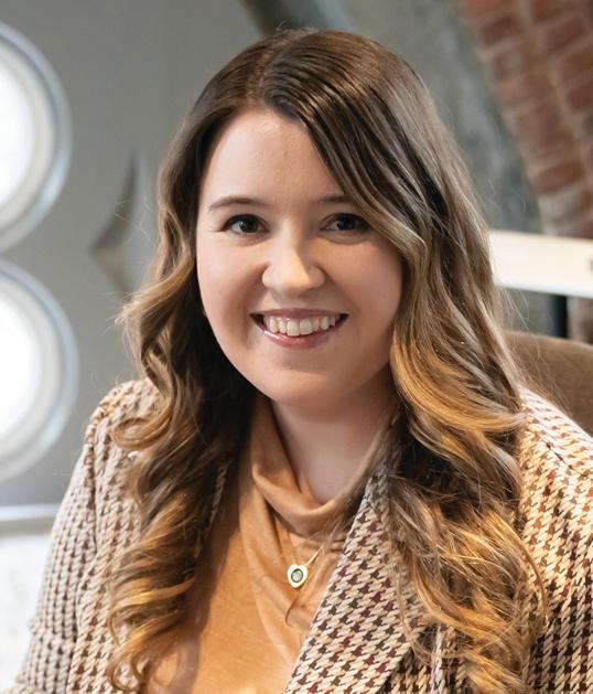 Photograph of a smiling woman with wavy brown hair wearing a plaid blazer.