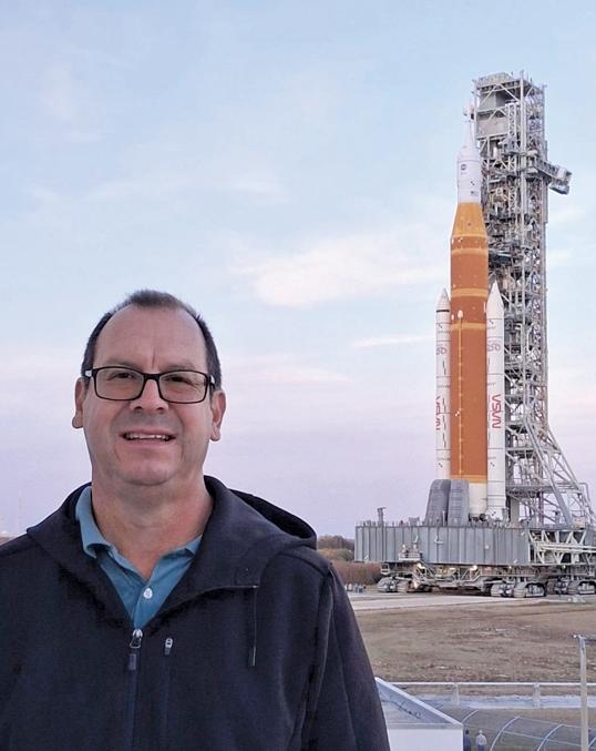 Photograph of a man smiling in front of the NASA Artemis rocket on its launch pad.