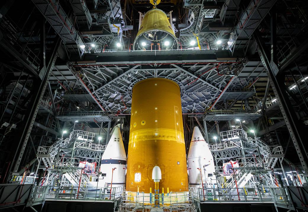 Photograph of the orange SLS core stage and boosters in a large assembly bay.