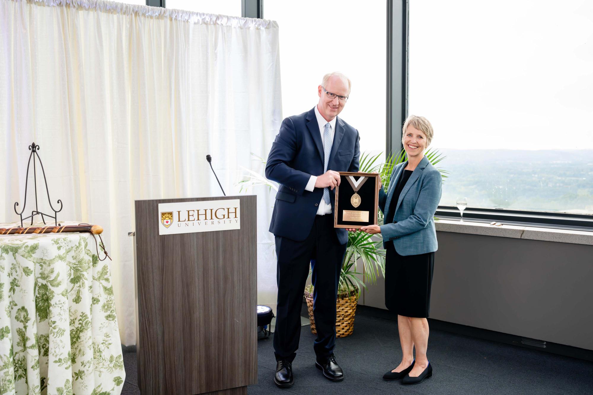 Man in a suit presenting an award plaque to a woman at a Lehigh University event.