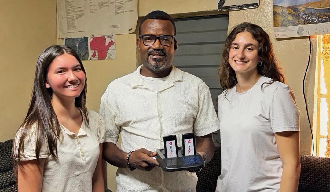Photograph of three smiling people holding a device with two smartphones.