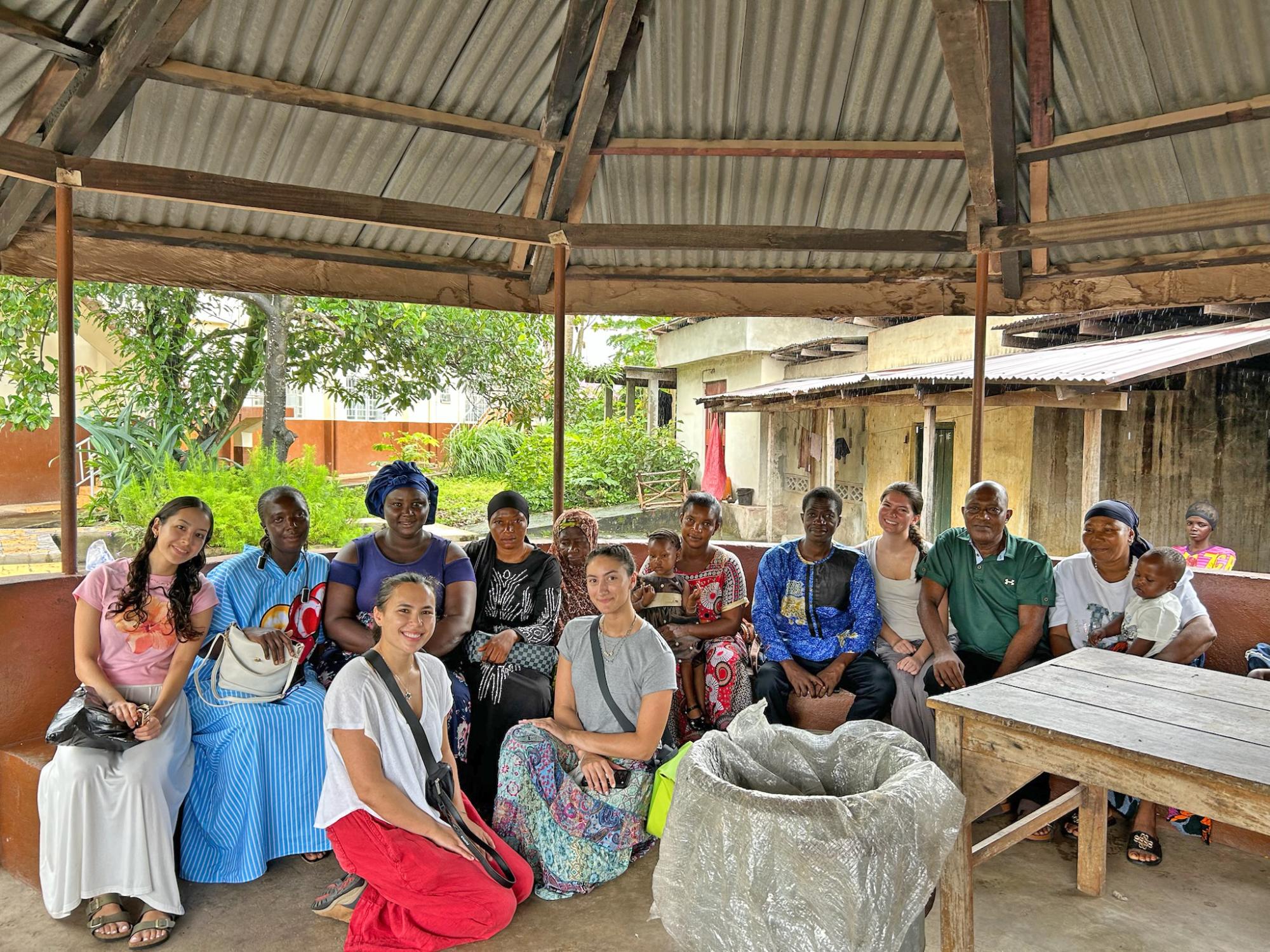 A group of people sitting together under a large gazebo with a corrugated metal roof.
