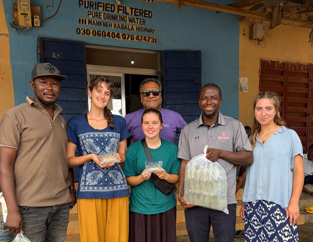 Diverse group of people posing with water sachets outside a purified water shop.