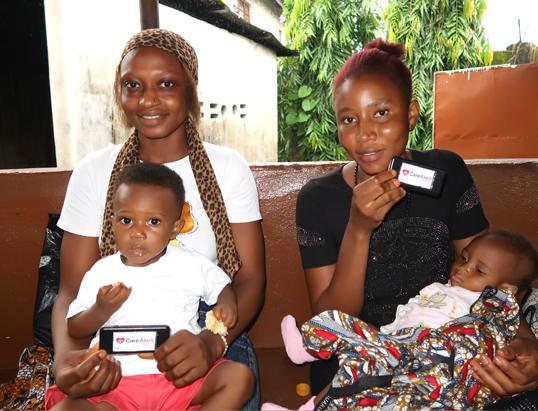 Photograph of two women and their children holding small devices with a red heart logo.