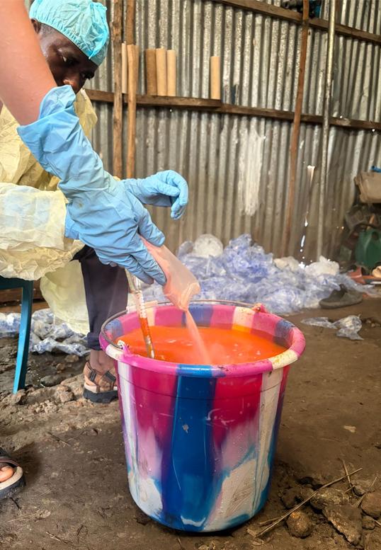 Photograph of a person in protective gear pouring orange liquid into a colorful bucket.