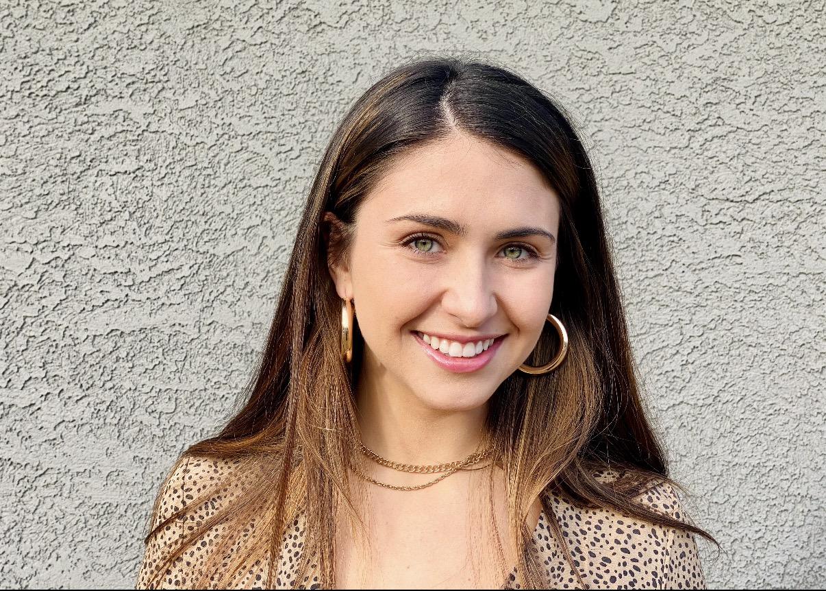 Photograph of a smiling woman with long brown hair, gold hoop earrings, and a leopard print top.