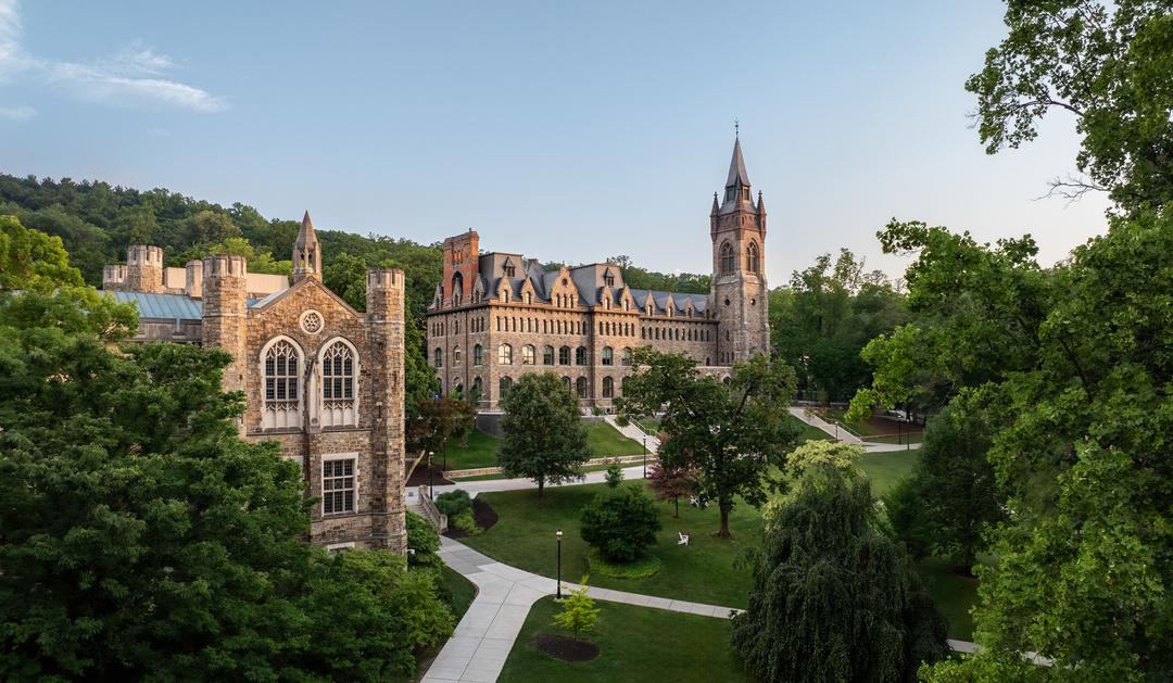Historic stone Linderman Library in the foreground and the Clayton University center with a tall tower in the background, on a green university campus shot from an aerial perspective.
