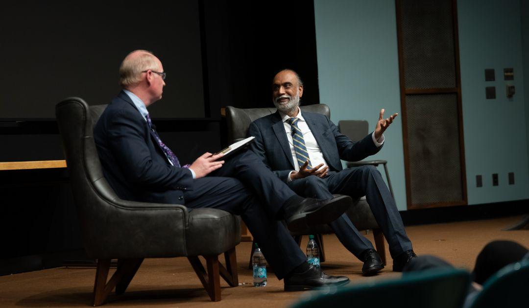 Photograph of two men in suits having a discussion on stage during a panel event.