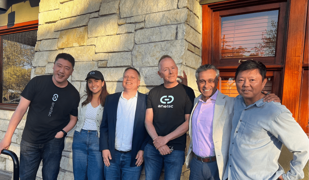 Photograph of six smiling people posing together in front of a stone wall.