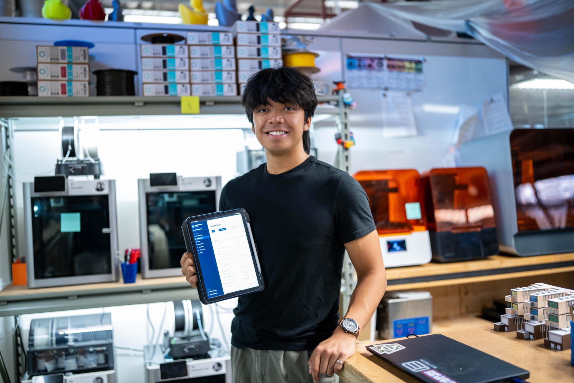 Photograph of a smiling man holding a tablet in a 3D printing workshop.