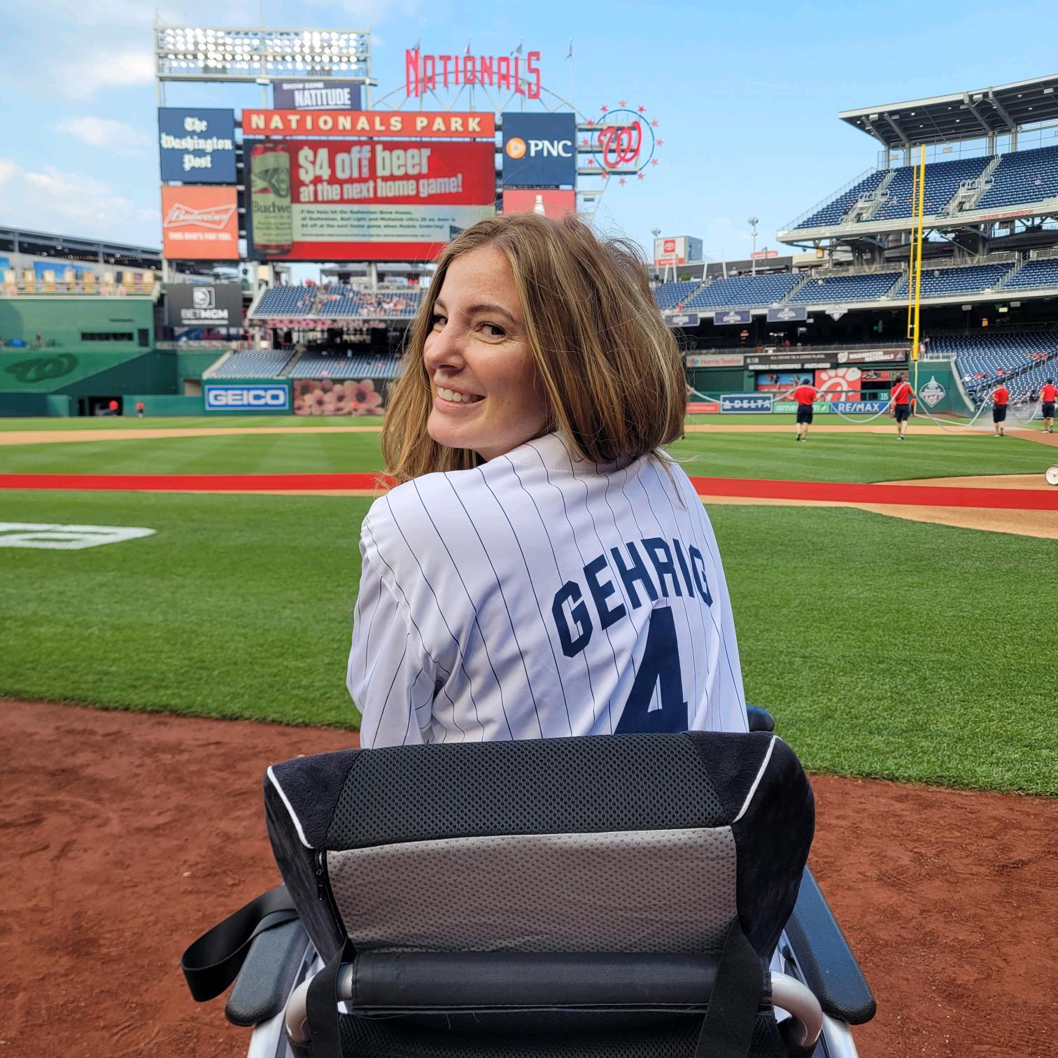 Smiling woman in a wheelchair at Nationals Park wearing a Lou Gehrig #4 pinstripe jersey.
