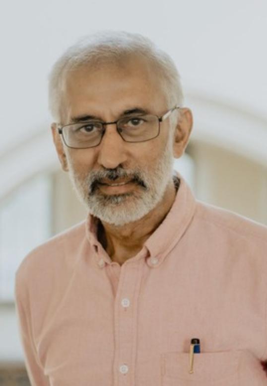 Photograph of a man wearing glasses and a pink shirt.
