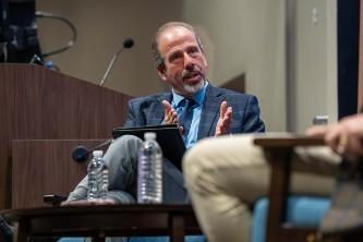 Photograph of a man in a suit gesturing while speaking during a discussion.