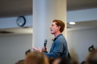 Photograph of a red-haired man speaking into a microphone during a presentation.