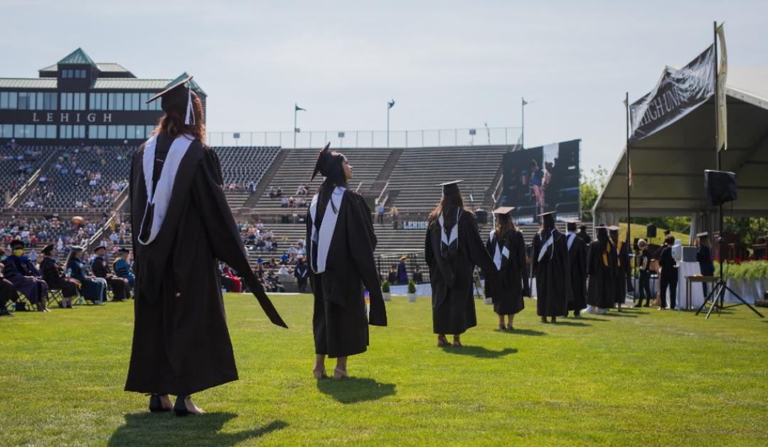 Graduates walk across the Goodman Stadium grass