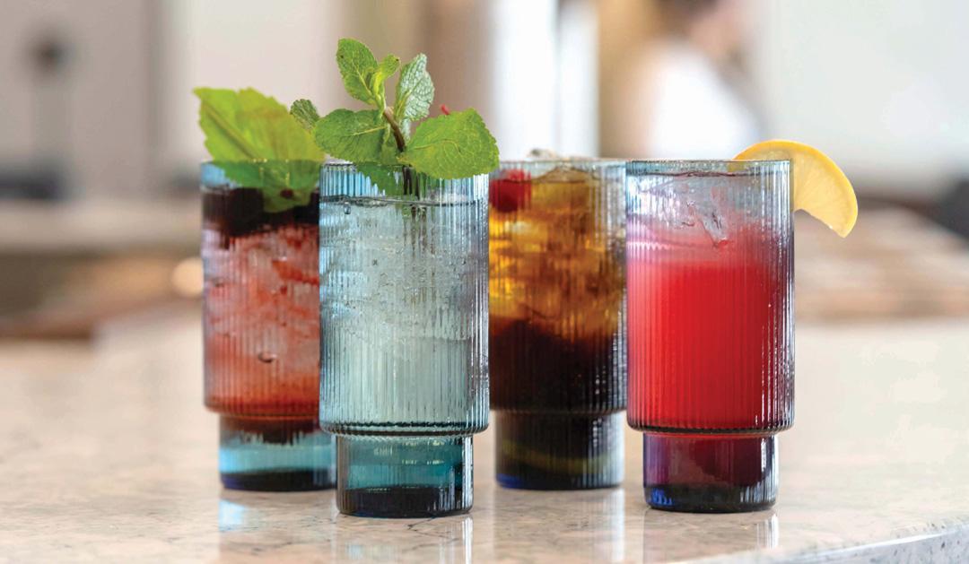 Four mocktails served in tall blue glasses arranged together on a tabletop.