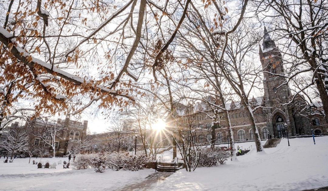 Snow-covered campus with leafless trees and sunlight peeking through, revealing the Clayton University Center.