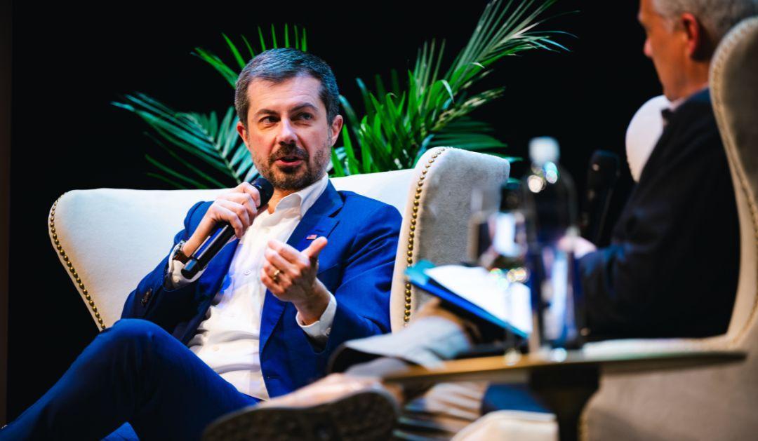 Pete Buttigieg in blue suit speaks into microphone at a seated event.