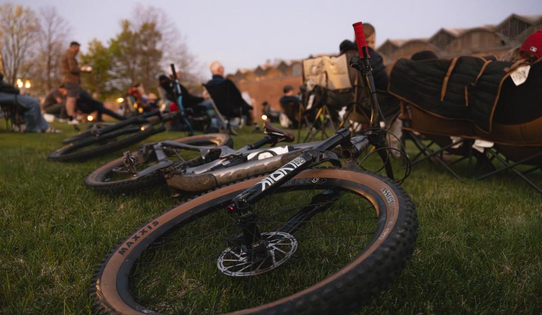 Photograph of mountain bikes on grass at an outdoor community event at dusk.