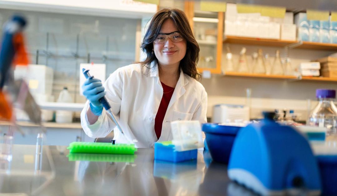 Photograph of Lillian Wu in a lab coat using a pipette in a laboratory.