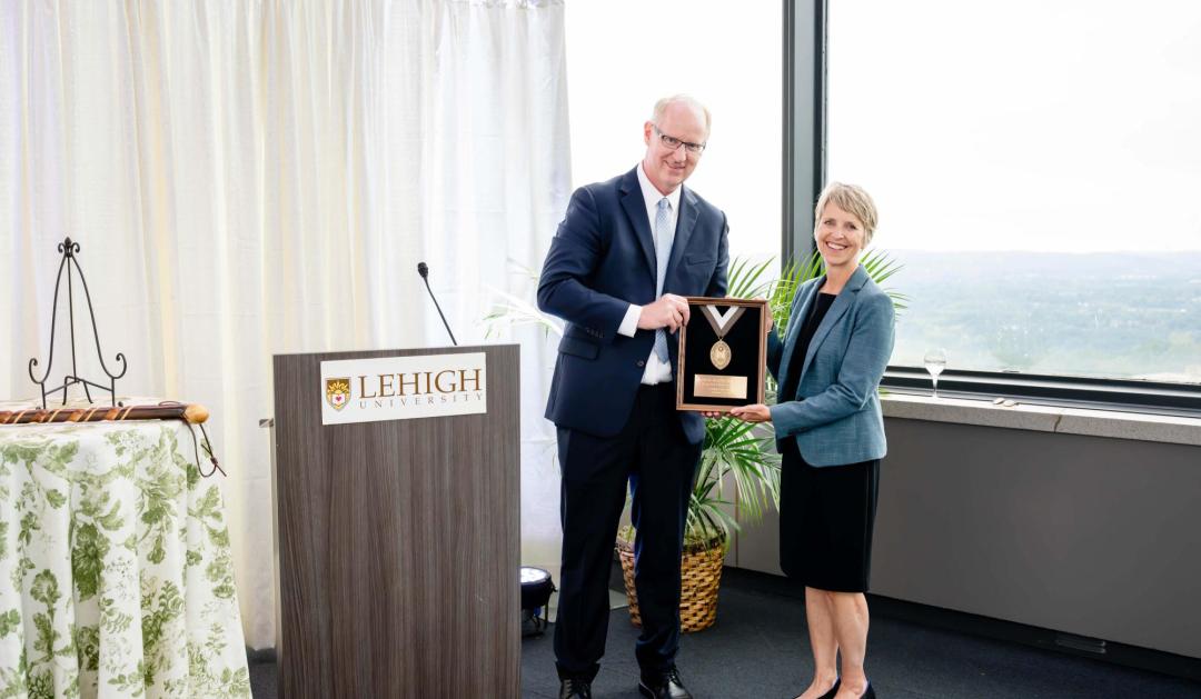 Photograph of a man presenting a framed plaque to a woman at a Lehigh University podium.