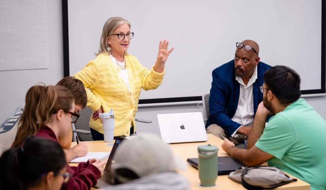 Woman in yellow sweater stands before university classroom, teaching