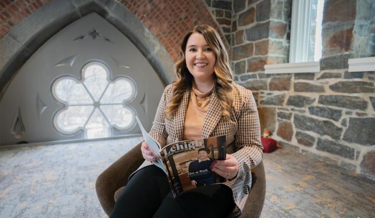 Editor holding a magazine while sitting in chair in campus building. 