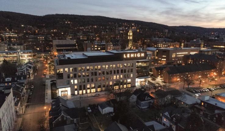 Twilight cityscape with illuminated buildings and hills in the background.