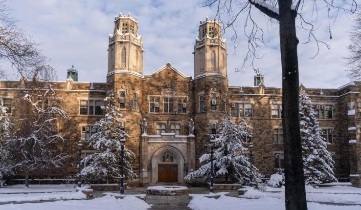 Snow-covered historical building with towers and trees.