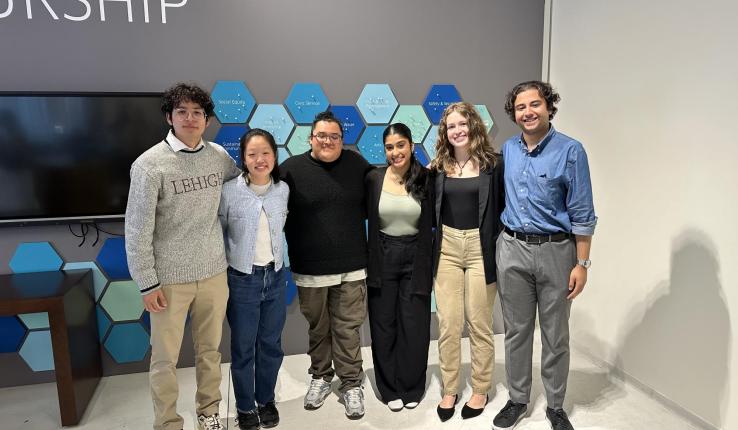 Photograph of six diverse young adults smiling in a modern office setting.