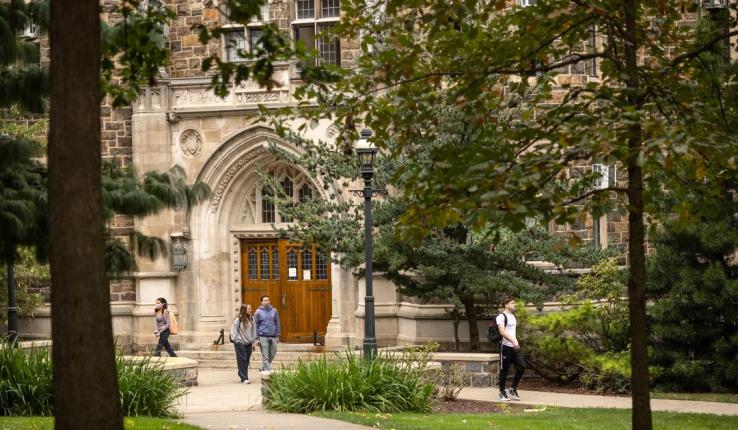 Photograph of students walking past a stone collegiate building with gothic arches.