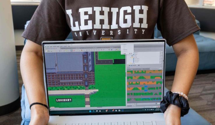 A student in a Lehigh University shirt holds a laptop showing a 2D game map editor.