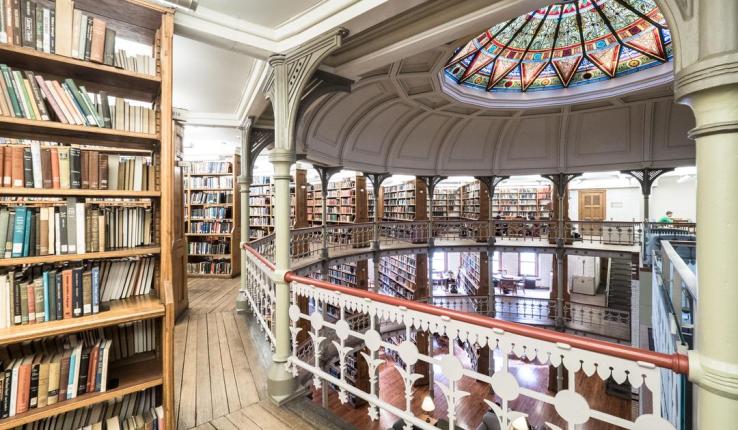 Historic circular library featuring a stained-glass dome, ornate balconies, and rows of books.