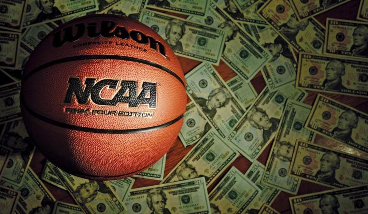 Wilson NCAA basketball resting on a pile of twenty-dollar bills.