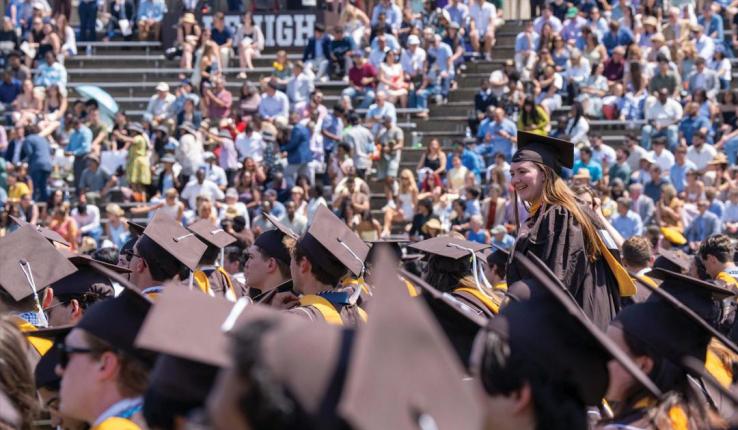 Photograph of graduates in brown and gold regalia at a crowded Lehigh University commencement.
