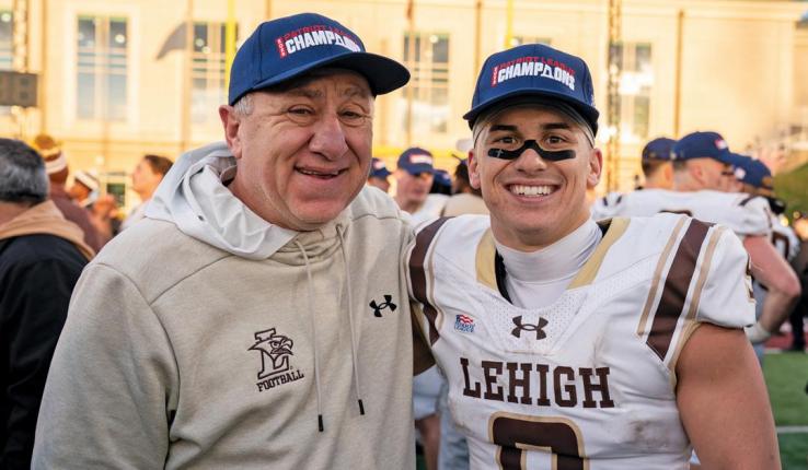 Photograph of a Lehigh football player and a man smiling in championship hats.