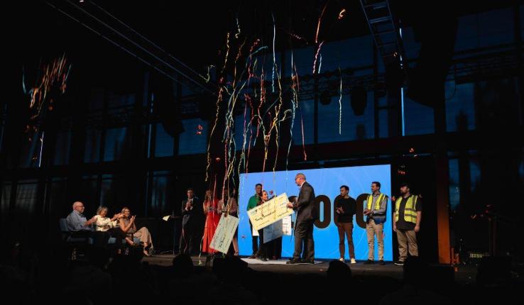 Photograph of people on stage celebrating with a giant check and falling streamers.