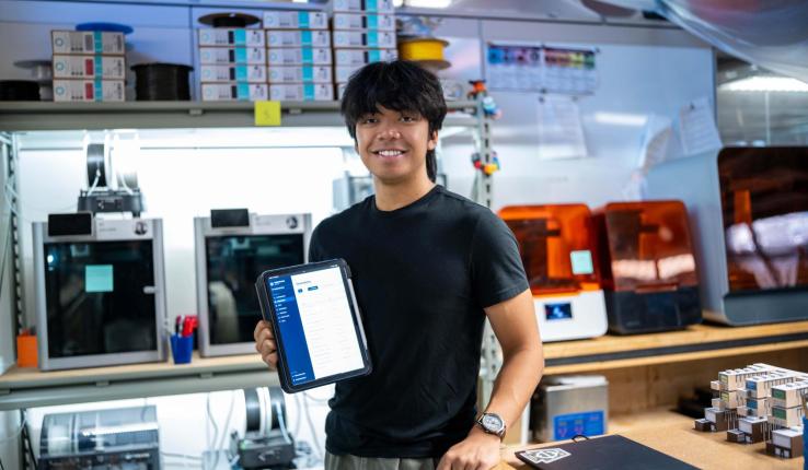 Photograph of a smiling man holding a tablet in a 3D printing workshop.