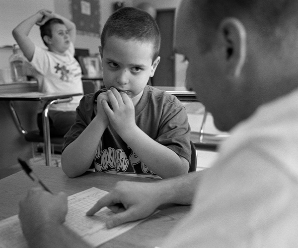 Teacher writing something on paper and explaining it to child sitting at the table